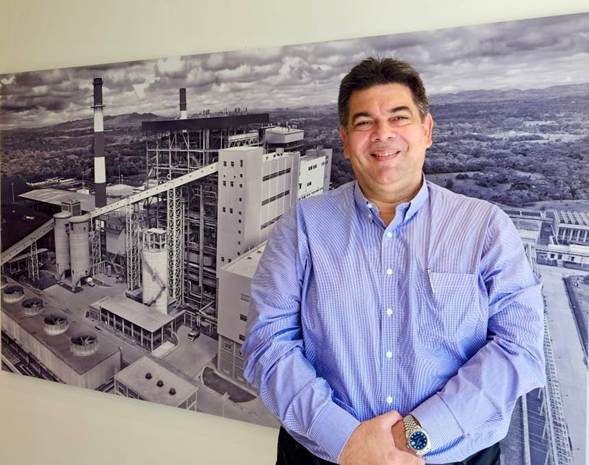 Los 2 italianos que junto al español amigo de Petro y Verónica Alcocer aparecen en el escándalo de Ecopetrol Smiling man in a blue button-down shirt standing in front of a large black-and-white industrial plant mural/photo behind him. - Los 2 italianos que junto al español amigo de Petro y Verónica Alcocer aparecen en el escándalo de Ecopetrol