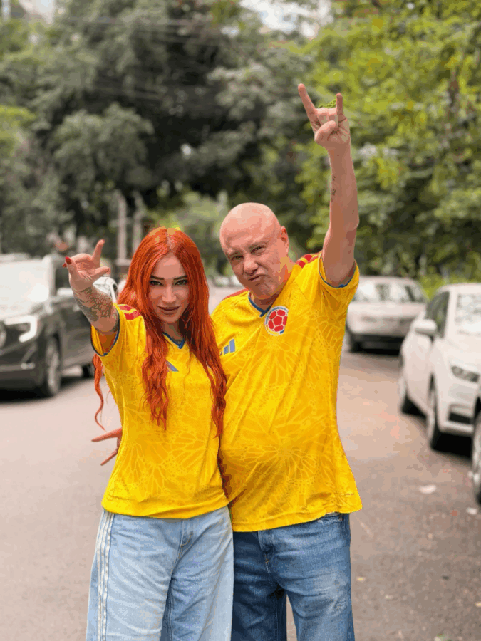 Two people in yellow sports jerseys pose on a street; the person on the left has red hair, the person on the right raises a rock-on hand gesture. - Quién es Alejandra Rosales, la DJ y periodista que conquistó a Jorge Rausch, famoso jurado de MasterChef