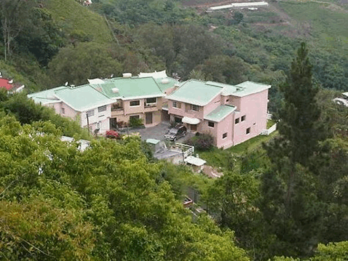 El derrumbe de Diosdado Cabello, quien ahora podría terminar en una cárcel en Santiago de Chile vinculado a un asesinato Pastel pink houses with green roofs on a hillside, surrounded by dense trees. - El derrumbe de Diosdado Cabello, quien ahora podría terminar en una cárcel en Santiago de Chile vinculado a un asesinato