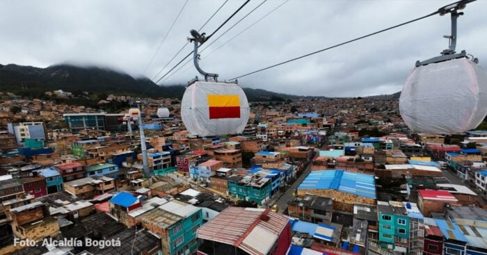 Dos familias ligadas al transporte bogotano junto a los bolivianos de Mi Teleférico operarán el cable de San Cristóbal Cable cars glide above a densely built hillside city with colorful rooftops and mountains in the background, Bogotá. - Dos familias ligadas al transporte bogotano junto a los bolivianos de Mi Teleférico operarán el cable de San Cristóbal