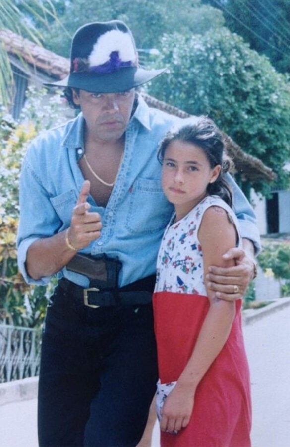 Luis Eduardo Arango, el actor paisa que se resiste a dejar la actuación en la que lleva más de medio siglo Man wearing a wide-brimmed hat and denim shirt stands close to a young girl in a red-and-white dress, arm around her, pointing at the camera outdoors. - Luis Eduardo Arango, el actor paisa que se resiste a dejar la actuación en la que lleva más de medio siglo