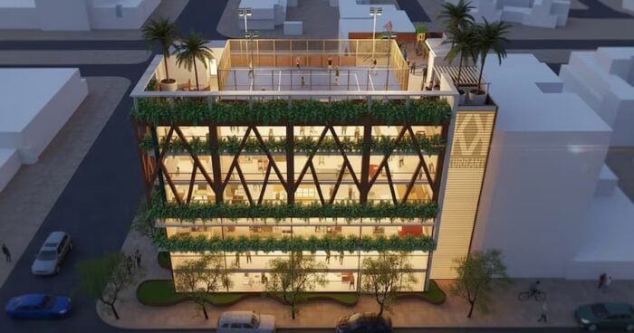 La reaparición de Andrés Camargo con un proyecto que sorprenderá en Bogotá A modern glass office building with diagonal wooden beams and three green terraces, topped by a rooftop terrace in an urban street scene. - La reaparición de Andrés Camargo con un proyecto que sorprenderá en Bogotá