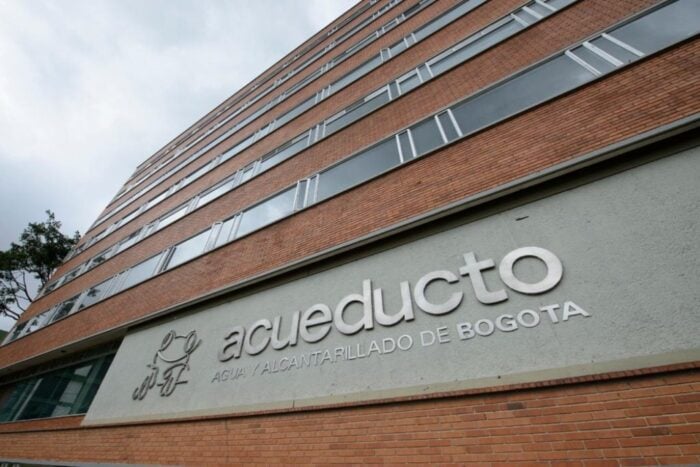 Brick building facade with a large gray sign reading 'acueducto' and 'AGUA Y ALCANTARILLADO DE BOGOTÁ' along the wall. - La Empresa de Acueducto de Bogotá busca el permiso de Minambiente para reutilizar las aguas residuales en industria