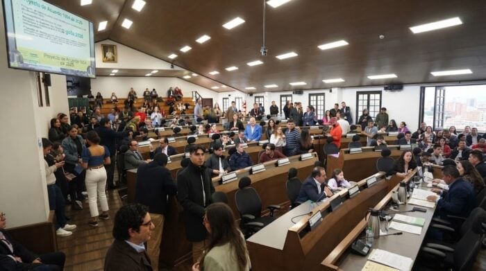 Los cuatro concejales de Bogotá que le salvaron a Galán el impuesto al alumbrado que 6 alcaldes no lograron Large council chamber with curved desks, many attendees seated and standing along the walls, engaging in discussions. - Los cuatro concejales de Bogotá que le salvaron a Galán el impuesto al alumbrado que 6 alcaldes no lograron