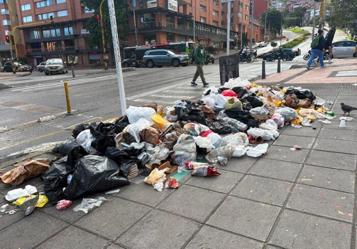 El fracasada estrategia de Galán para limpiar la ciudad de basuras que ha costado .000 millones y no ha servido A long pile of trash bags and loose litter spilling onto a city sidewalk with cars and pedestrians in the background. - El fracasada estrategia de Galán para limpiar la ciudad de basuras que ha costado .000 millones y no ha servido
