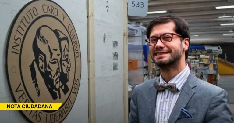 Man in a gray blazer and bow tie stands beside a large circular seal that reads Instituto Caro y Cuervo in a library setting, smiling at the camera. - ¿El Instituto Caro y Cuervo pasó de la investigación literaria a la censura moral?