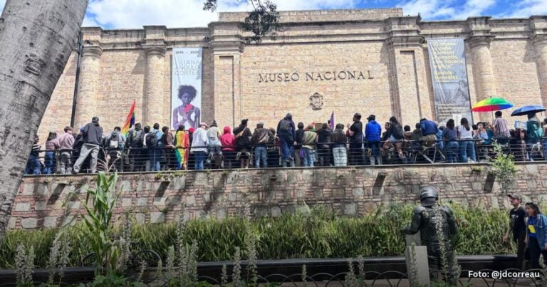 Las2orillas.co: Historias, voces y noticias de Colombia Crowd lines a railing outside Museo Nacional, some holding banners and a rainbow flag against a brick facade. - Las2orillas.co: Historias, voces y noticias de Colombia