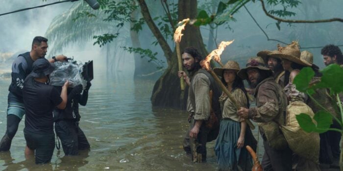 Así fue como Netflix convirtió a Macondo en un negocio que le dejó más de medio billón de pesos a Colombia Film crew filming a group of indigenous people standing in a muddy swamp with torches and trees in the background.