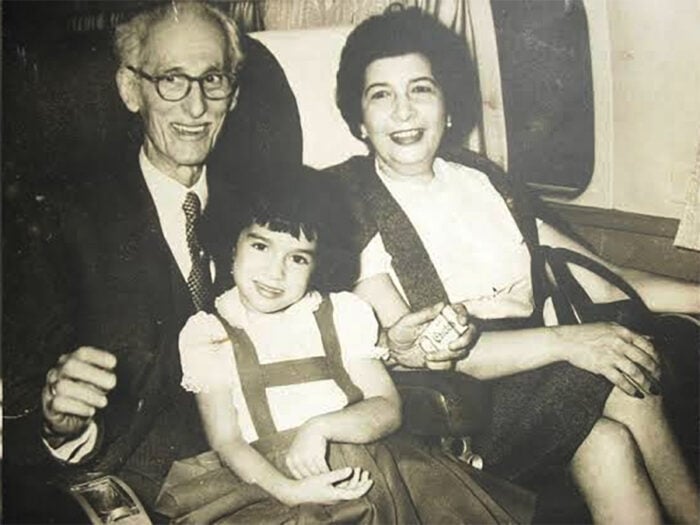 Three-generation family posing together on an airplane: a smiling elderly man with glasses, a smiling woman, and a young girl in a dress seated between them. - Así es la mansión en Bogotá de Leo Kopp, el fundador de Bavaria, que terminó convertida en el templo de los masones