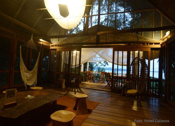 El hotel de lujo que el pintor Diego Samper levantó en la selva del Amazonas desde hace 40 años Open-air wooden lounge area with a hammock, hanging chair, and draped curtains leading to a seaside veranda at dusk; cozy, tropical retreat atmosphere. - El hotel de lujo que el pintor Diego Samper levantó en la selva del Amazonas desde hace 40 años