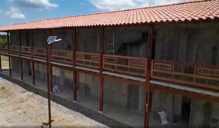 La Federación de Cafeteros se mete al negocio hotelero con un megaproyecto frente al Parque del Café Two-story concrete building with a red-tiled roof and wooden balcony railings, under a sunny blue sky; a solar panel is mounted on a pole nearby. - La Federación de Cafeteros se mete al negocio hotelero con un megaproyecto frente al Parque del Café