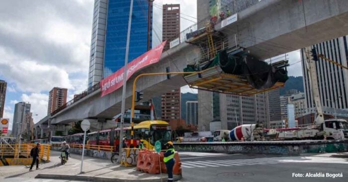 Luz verde del Tigre para que los bogotanos empiecen a soñar con la Línea 4 del metro Construction site under an elevated track in downtown Bogotá; workers in safety vests with a cement mixer and traffic barriers nearby. - Luz verde del Tigre para que los bogotanos empiecen a soñar con la Línea 4 del metro
