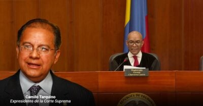 Las2orillas.co: Historias, voces y noticias de Colombia Portrait of Camilo Tarquino, former president of the Supreme Court, in a suit with a judge at a desk in a courtroom behind him, featuring a Colombian flag. - Las2orillas.co: Historias, voces y noticias de Colombia