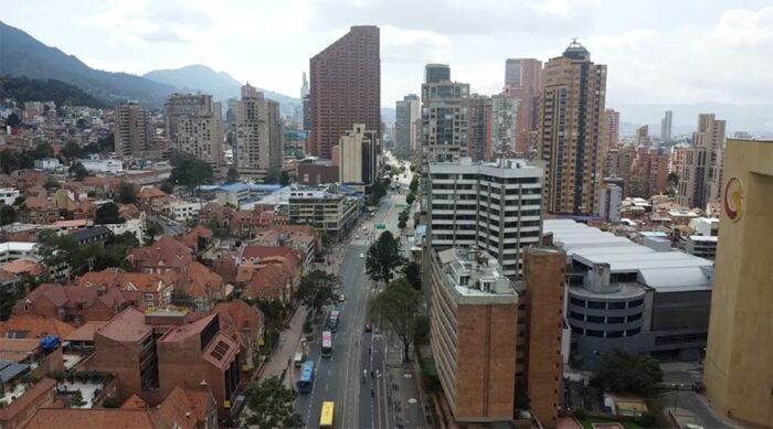 El barrio más ‘cool’ de América Latina lo tiene Bogotá y vivir allá no es barato City skyline with tall buildings along a central road, red-roofed houses, and distant mountains. - El barrio más ‘cool’ de América Latina lo tiene Bogotá y vivir allá no es barato