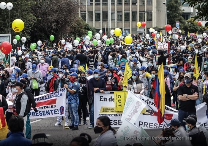 Por qué pelean entre ellos los 21 miembros del comité ejecutivo nacional de la Central Unitaria de Trabajadores Large street protest with a dense crowd of masked demonstrators holding banners and balloons in a city setting. - Por qué pelean entre ellos los 21 miembros del comité ejecutivo nacional de la Central Unitaria de Trabajadores