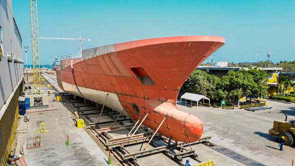 Colombia se mete en las grandes ligas navales y en Cartagena construye su primer buque de guerra de ,6 billones Large orange ship hull on a dry dock under construction/maintenance, supported by scaffolding with cranes and yard equipment nearby. - Colombia se mete en las grandes ligas navales y en Cartagena construye su primer buque de guerra de ,6 billones