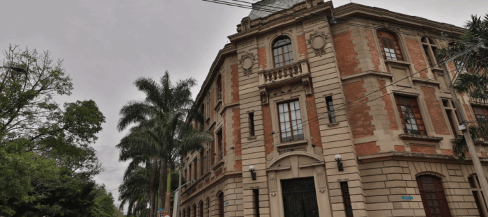 El médico Francisco Lopera y otros 15 científicos de la U. de Antioquia se metieron entre los más influyentes del mundo Historic brick and stone building with ornate facade and arched windows, surrounded by palm trees under a cloudy sky. - El médico Francisco Lopera y otros 15 científicos de la U. de Antioquia se metieron entre los más influyentes del mundo