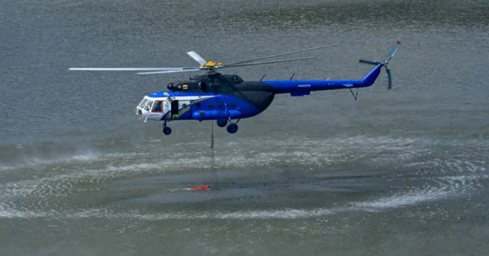 El piloto que lidera una empresa de aviación que se convirtió en la más grande de vuelos en helicópteros y jets privados Blue rescue helicopter hovers over water releasing a red water bucket for firefighting a lake scene - El piloto que lidera una empresa de aviación que se convirtió en la más grande de vuelos en helicópteros y jets privados