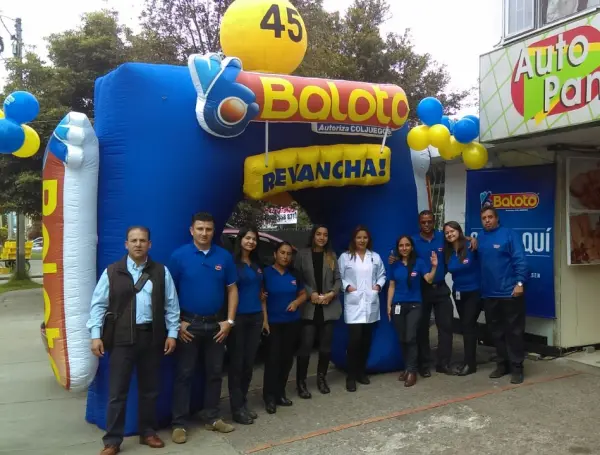 Baloto cayó en un pequeño pueblo de Boyacá, el departamento donde hace diez años no caía el premio gordo Group of staff in blue uniforms posing in front of a large blue Baloto inflatable booth with a yellow ball on top and banners reading 'Reváncha' outdoors at a street event far from a shop. - Baloto cayó en un pequeño pueblo de Boyacá, el departamento donde hace diez años no caía el premio gordo