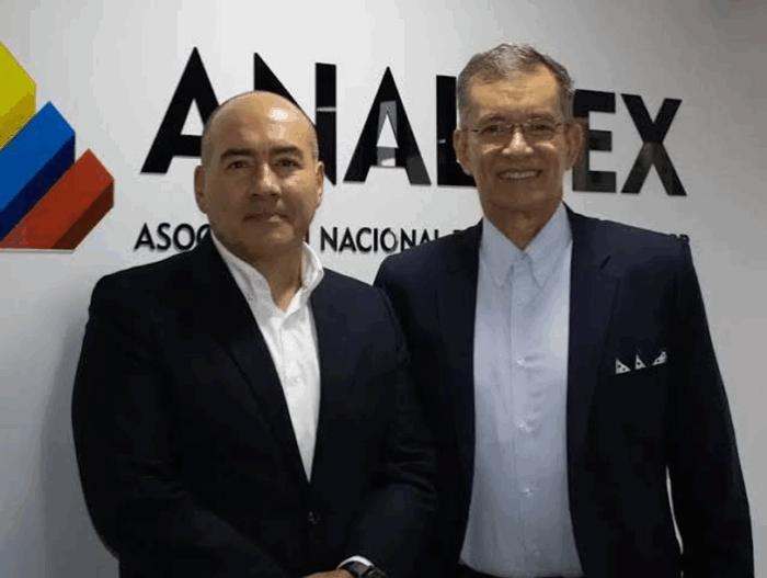 Two men in suits pose for a photo in front of a wall with a colorful logo and the word ANALABEX partially visible. - La sacudida en los gremios empresariales que mandan: Bruce Mac Master sale de la Andi y Javier Díaz deja Analdex
