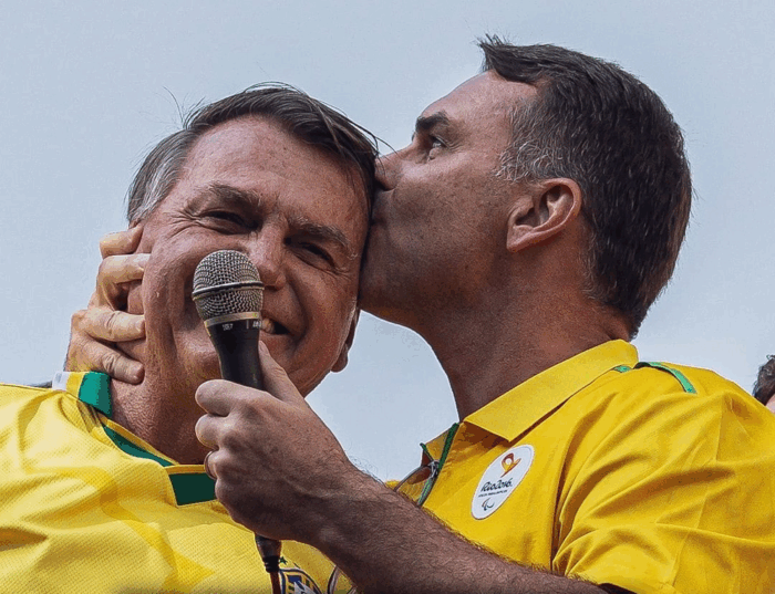 Brasil decide si se queda con Lula o vuelve a la presidencia un Bolsonaro Two men in yellow jerseys share a hug; one kisses the other on the cheek while holding a microphone at a event. - Brasil decide si se queda con Lula o vuelve a la presidencia un Bolsonaro