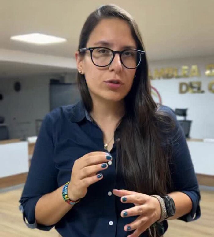 El proyecto turístico de 0 mil millones que le frenaron a los dueños de Panaca en el Quindío Woman with long dark hair and glasses gestures while speaking in a navy button-down shirt in a modern office lobby/backdrop signage visible behind her. - El proyecto turístico de 0 mil millones que le frenaron a los dueños de Panaca en el Quindío