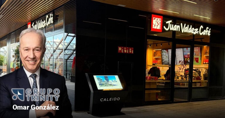 Las2orillas.co: Historias, voces y noticias de Colombia Smiling man in a suit stands outside a Juan Valdez Café storefront with a touchscreen information kiosk nearby and Grupo Trinity branding visible. - Las2orillas.co: Historias, voces y noticias de Colombia