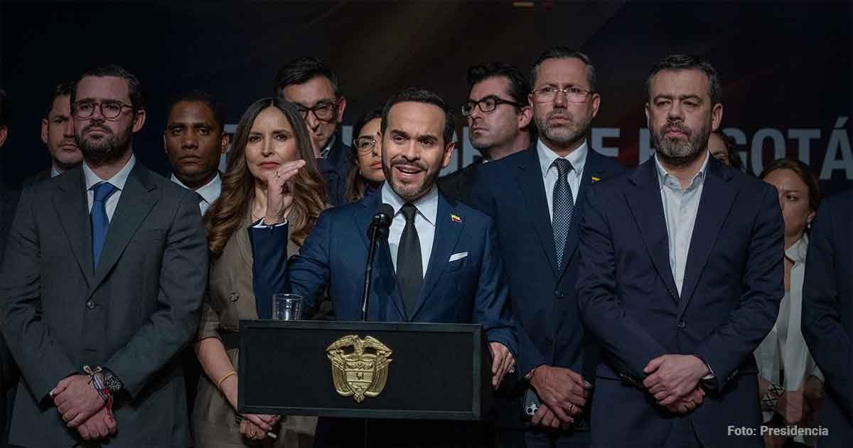 Man in blue suit speaking at a lectern with a crest, flanked by delegates in business attire behind him at a formal event. - Luz verde del Tigre para que los bogotanos empiecen a soñar con la Línea 4 del metro
