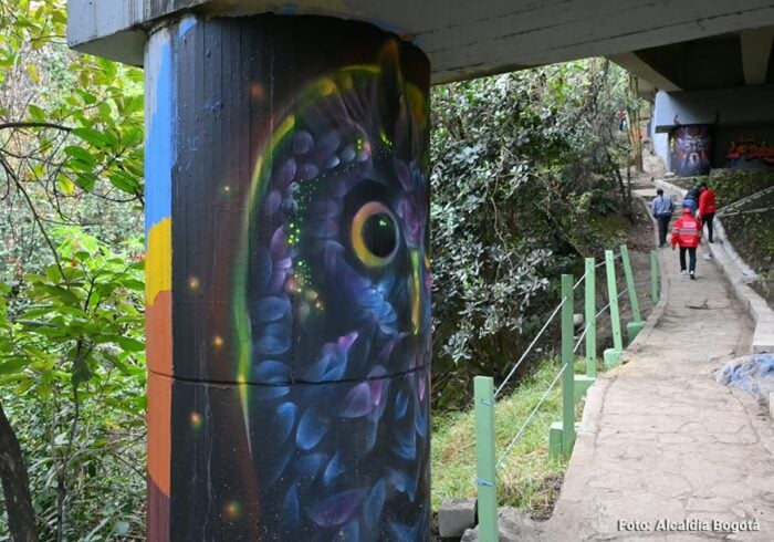 El sendero turístico que lleva a las montañas de Bogotá al que Galán le metió 0 millones para recuperarlo Painted pillar under a bridge with abstract blue and purple artwork, a concrete walkway, and hikers in the background. - El sendero turístico que lleva a las montañas de Bogotá al que Galán le metió 0 millones para recuperarlo
