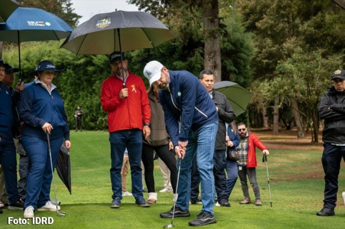 Cómo logró Galán recuperar el campo de golf del Parque La Florida para que se pueda jugar sin gastar mucha plata Group of people under umbrellas watching a man in a cap prepare to golf on a green fairway. - Cómo logró Galán recuperar el campo de golf del Parque La Florida para que se pueda jugar sin gastar mucha plata