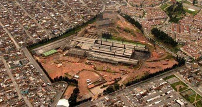 Moore: la fábrica de tubos y ladrillos que desapareció para darle paso al Portal 20 de julio Aerial view of a fenced construction site with a long, low building complex, red dirt around it, surrounded by dense urban housing. - Moore: la fábrica de tubos y ladrillos que desapareció para darle paso al Portal 20 de julio