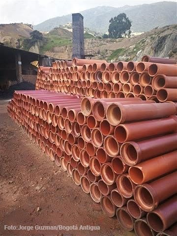 Moore: la fábrica de tubos y ladrillos que desapareció para darle paso al Portal 20 de julio Stacks of orange pipes piled outdoors at a construction site, with a dirt ground and hills in the background. - Moore: la fábrica de tubos y ladrillos que desapareció para darle paso al Portal 20 de julio